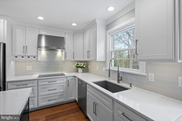kitchen featuring white cabinets, a sink, stainless steel appliances, light countertops, and wall chimney exhaust hood