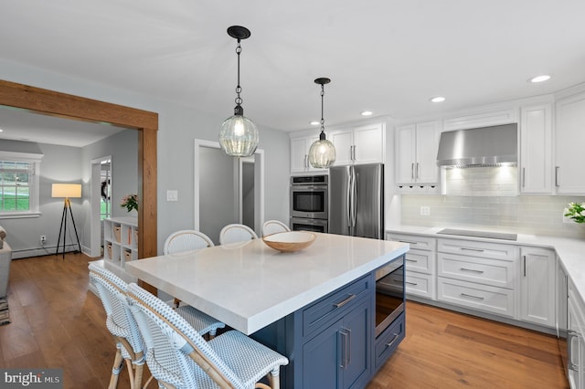 kitchen featuring wall chimney range hood, white cabinetry, appliances with stainless steel finishes, blue cabinets, and light countertops