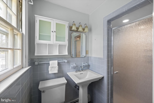 bathroom with toilet, plenty of natural light, a stall shower, and tile walls