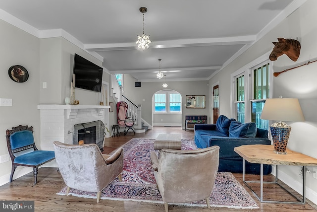 living area with a fireplace, baseboards, wood finished floors, stairway, and beam ceiling