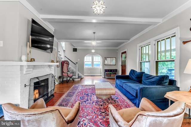 living area with a fireplace, beam ceiling, stairs, wood finished floors, and crown molding
