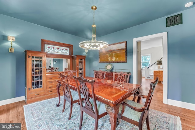 dining space with a chandelier, baseboards, wood finished floors, and stairway