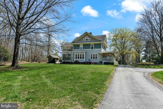 view of front facade with a porch, a front lawn, a chimney, and driveway