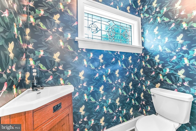 half bathroom featuring wallpapered walls, toilet, vanity, and baseboards