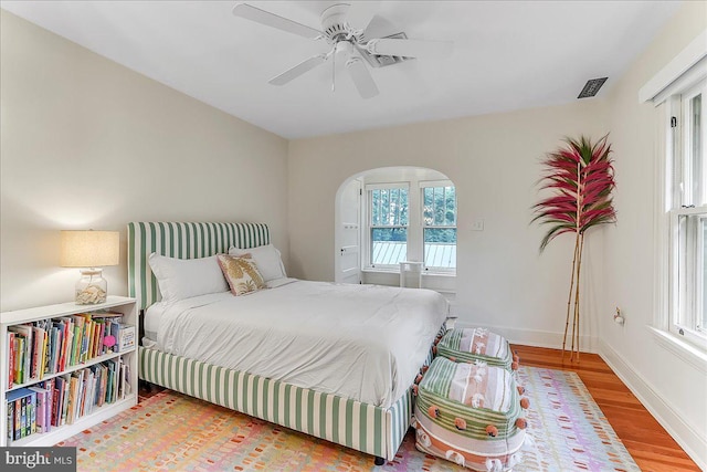 bedroom featuring wood finished floors, baseboards, arched walkways, and a ceiling fan