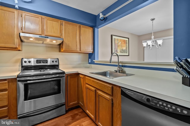 kitchen featuring under cabinet range hood, wood finished floors, light countertops, a sink, and stainless steel appliances