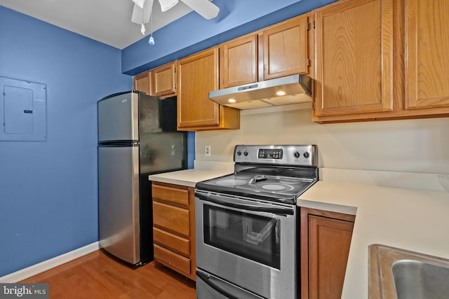 kitchen featuring electric panel, under cabinet range hood, wood finished floors, light countertops, and stainless steel appliances
