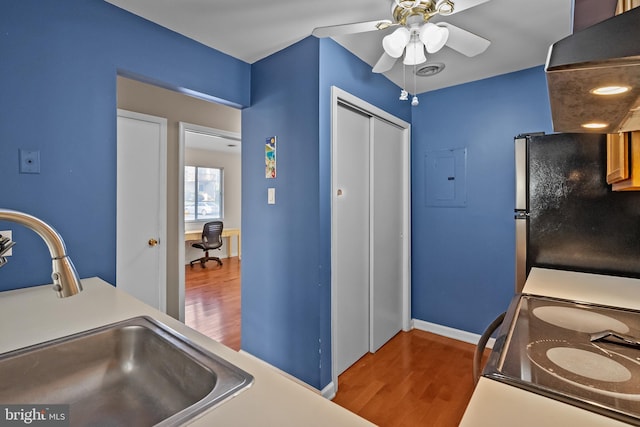 kitchen featuring freestanding refrigerator, a ceiling fan, electric panel, wood finished floors, and a sink