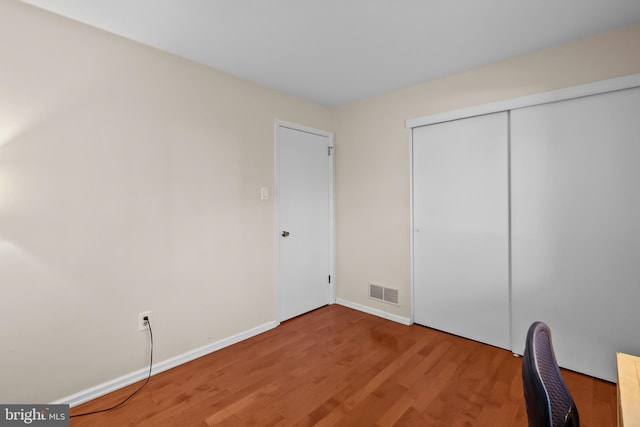 unfurnished bedroom featuring visible vents, baseboards, a closet, and wood finished floors