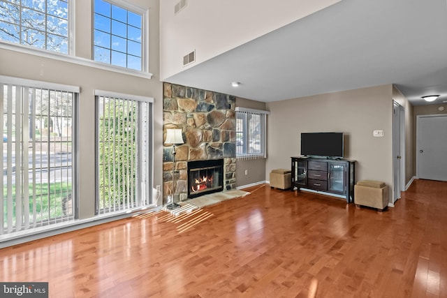 living room featuring visible vents, a stone fireplace, wood finished floors, and baseboards