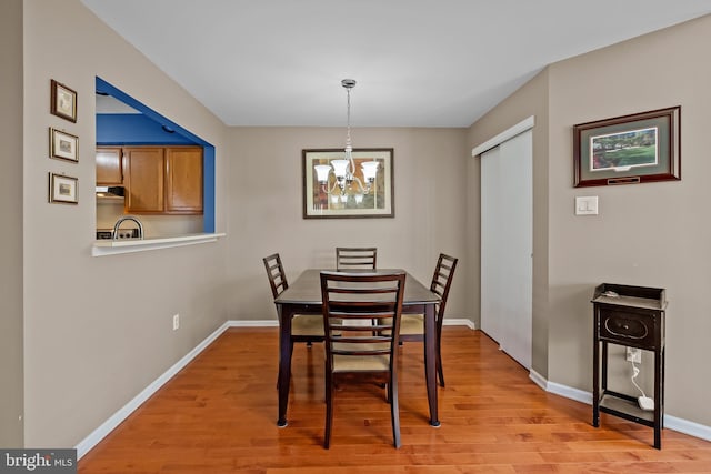 dining area with baseboards, light wood-type flooring, and a notable chandelier