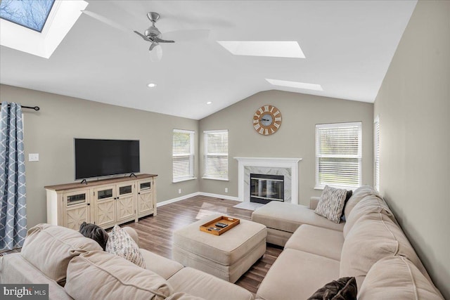 living room featuring baseboards, a ceiling fan, a premium fireplace, lofted ceiling with skylight, and wood finished floors
