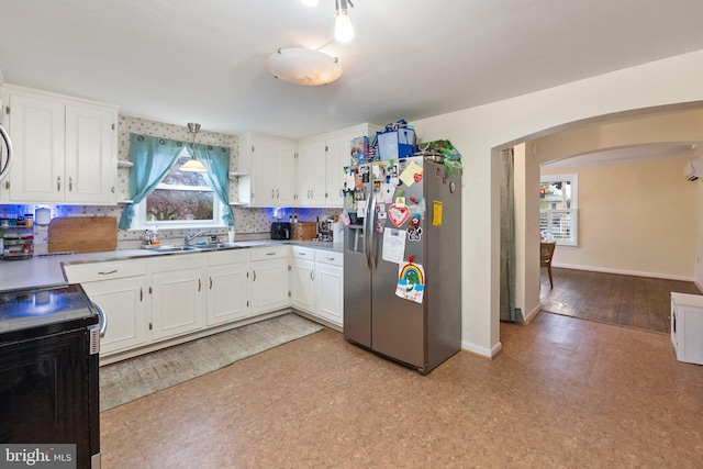 kitchen with stainless steel fridge with ice dispenser, arched walkways, white cabinets, a sink, and baseboards