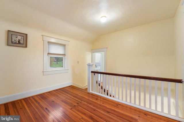 empty room featuring wood-type flooring, baseboards, and vaulted ceiling
