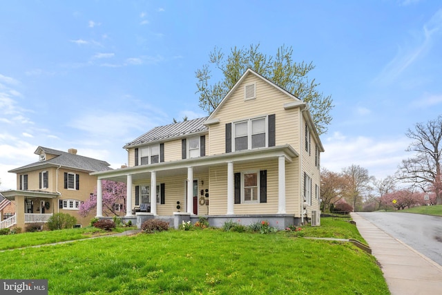 traditional home featuring a porch, a standing seam roof, a front yard, and metal roof