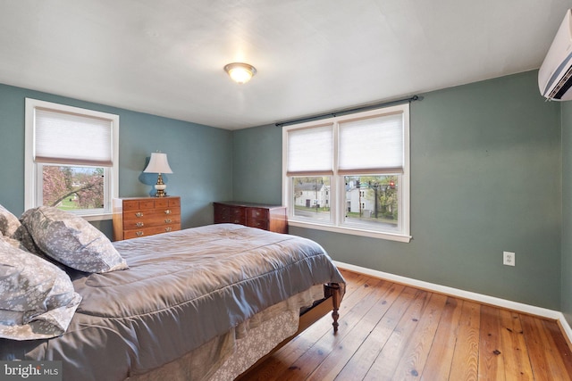 bedroom with a wall unit AC, baseboards, multiple windows, and hardwood / wood-style flooring