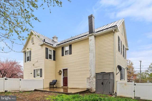 back of property featuring a standing seam roof, metal roof, fence, a gate, and a chimney