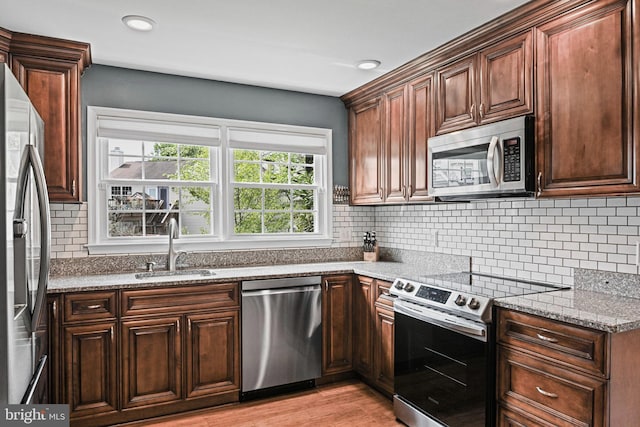 kitchen featuring light stone counters, a sink, light wood-style floors, stainless steel appliances, and tasteful backsplash