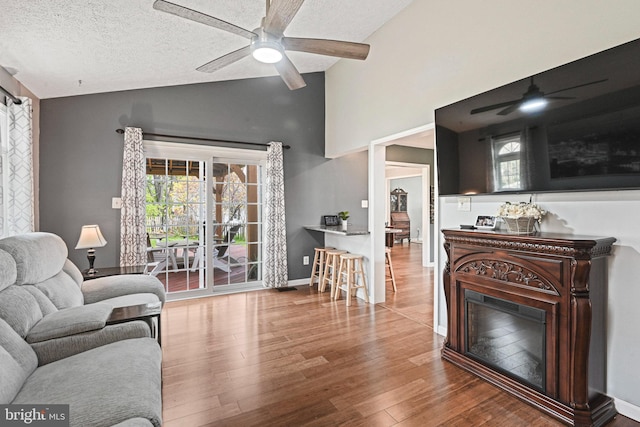 living area with high vaulted ceiling, ceiling fan, a textured ceiling, and wood finished floors