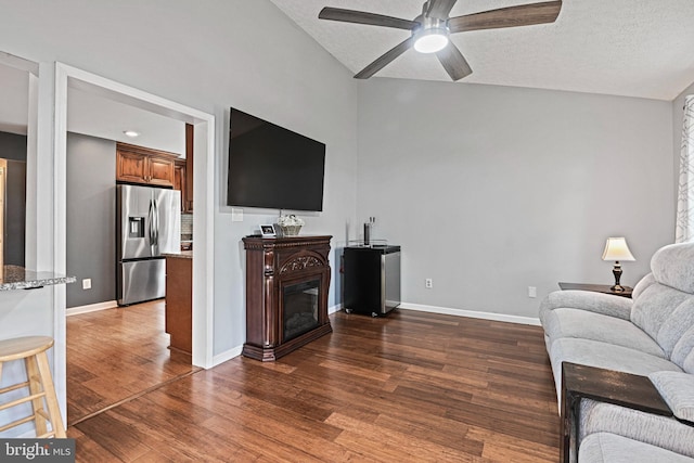 living room featuring ceiling fan, dark wood finished floors, a glass covered fireplace, baseboards, and lofted ceiling