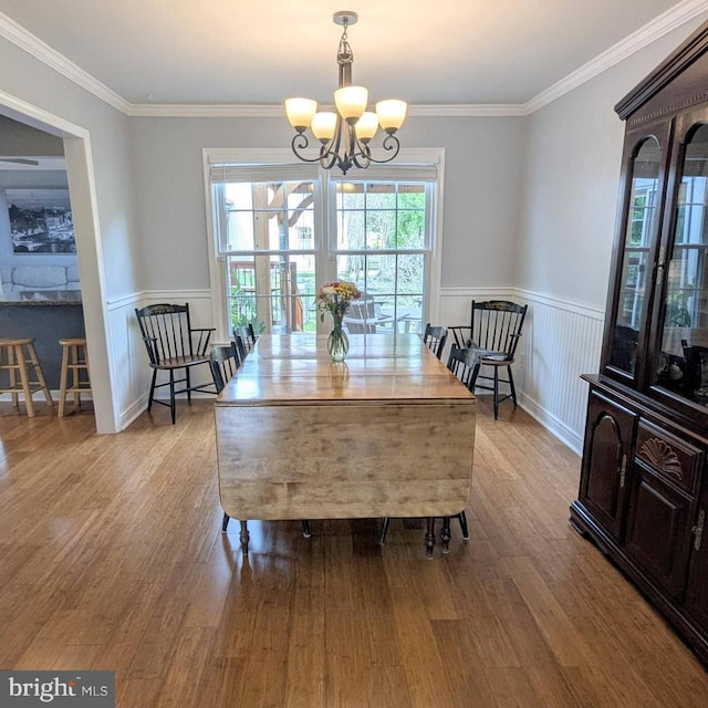 dining space featuring crown molding, wainscoting, wood finished floors, and a notable chandelier