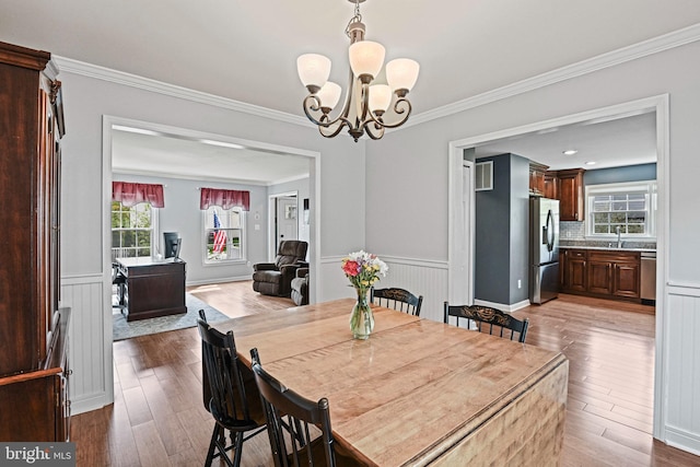 dining area with ornamental molding, wainscoting, wood finished floors, and a notable chandelier
