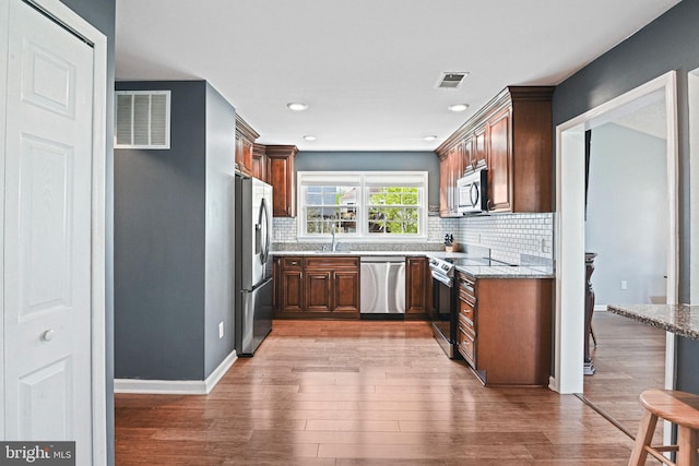 kitchen with appliances with stainless steel finishes, backsplash, light wood-style flooring, and visible vents