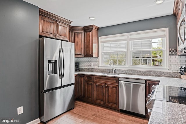 kitchen featuring a healthy amount of sunlight, light wood-type flooring, tasteful backsplash, a sink, and stainless steel appliances