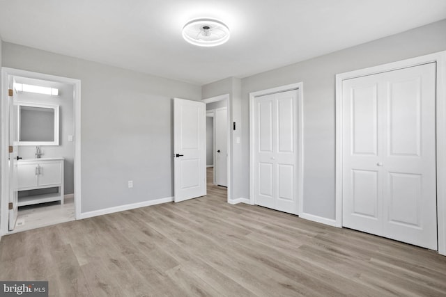 unfurnished bedroom featuring ensuite bathroom, multiple closets, light wood finished floors, and baseboards