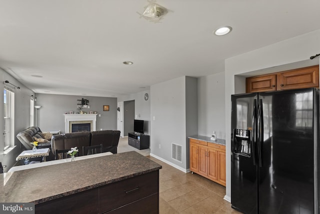 kitchen with dark countertops, visible vents, black refrigerator with ice dispenser, a fireplace, and light tile patterned floors
