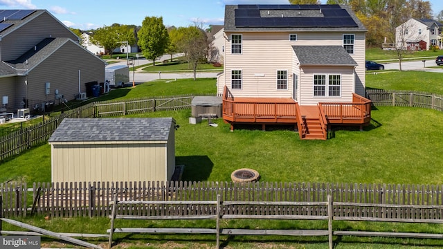 rear view of house with a storage unit, a fenced backyard, a deck, an outdoor structure, and a yard