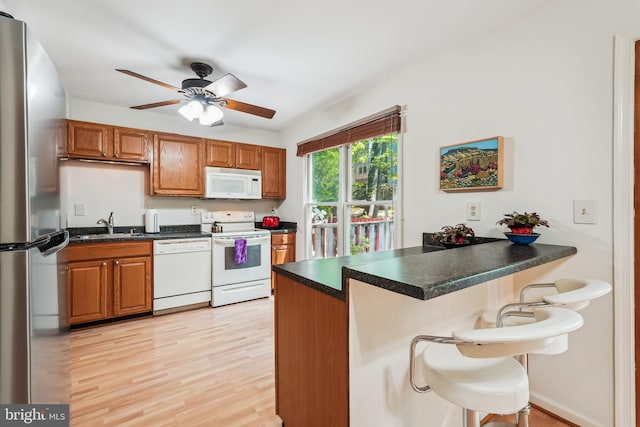 kitchen featuring a peninsula, a breakfast bar area, dark countertops, ceiling fan, and white appliances