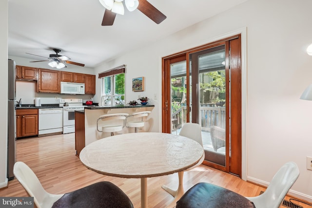 dining space with a ceiling fan, baseboards, and light wood-type flooring