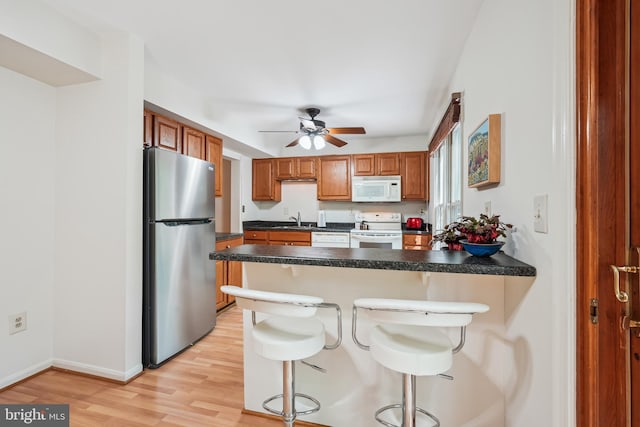 kitchen featuring a peninsula, brown cabinets, a sink, ceiling fan, and white appliances