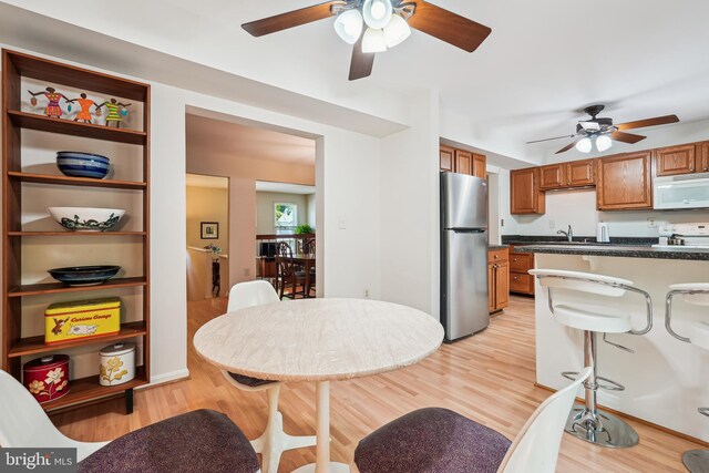 kitchen featuring a sink, brown cabinetry, white appliances, a ceiling fan, and dark countertops