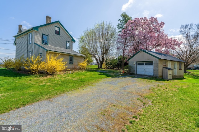 view of side of home featuring an outbuilding, a yard, a detached garage, a chimney, and driveway
