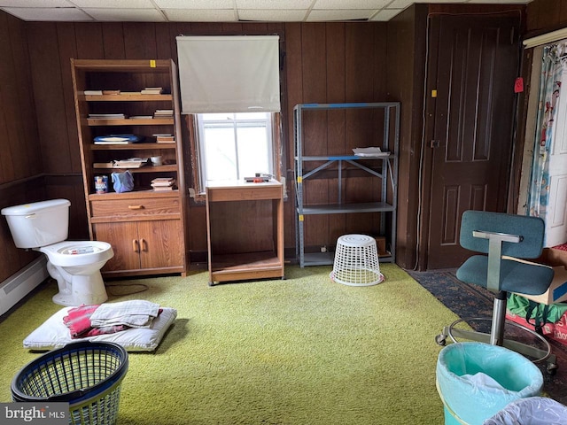 interior space featuring a paneled ceiling, a baseboard heating unit, wooden walls, and carpet floors