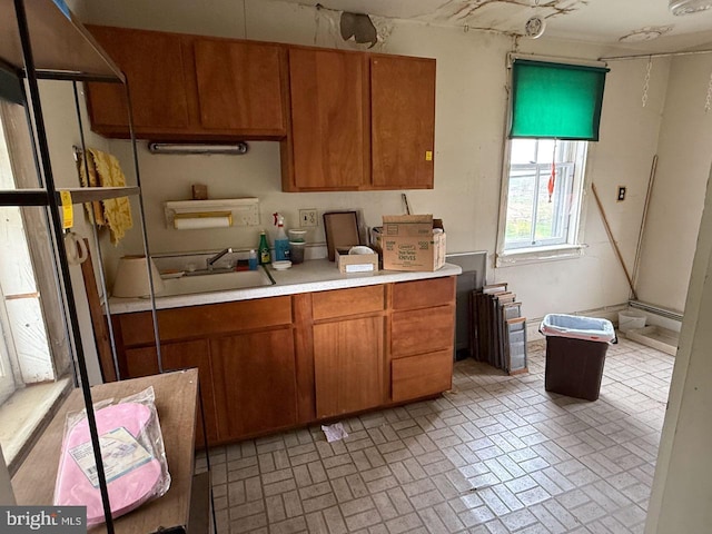 kitchen featuring light countertops, brown cabinetry, a sink, and brick patterned floor
