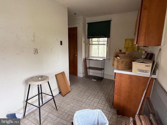 kitchen featuring brown cabinets, light countertops, baseboards, and brick patterned floor