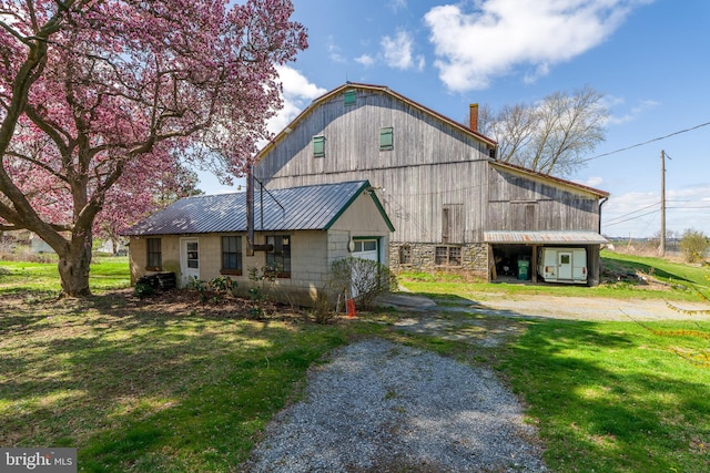 view of front of home with a front yard, a barn, a detached garage, metal roof, and an outdoor structure