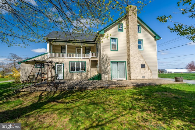 rear view of house featuring a patio area, a chimney, a yard, and a balcony