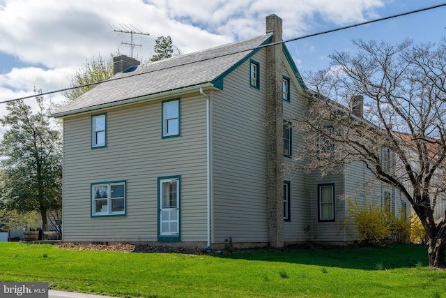 view of side of property with a chimney, a shingled roof, and a lawn