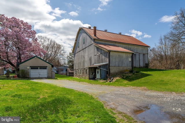 view of side of home featuring a barn, a garage, a lawn, dirt driveway, and an outbuilding