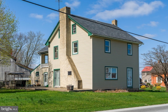 rear view of house with a patio, a chimney, a shingled roof, and a yard