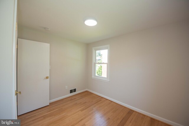empty room with light wood finished floors, visible vents, and baseboards
