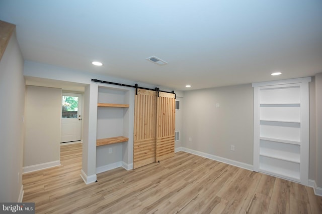 unfurnished bedroom with light wood-style flooring, visible vents, recessed lighting, a barn door, and baseboards