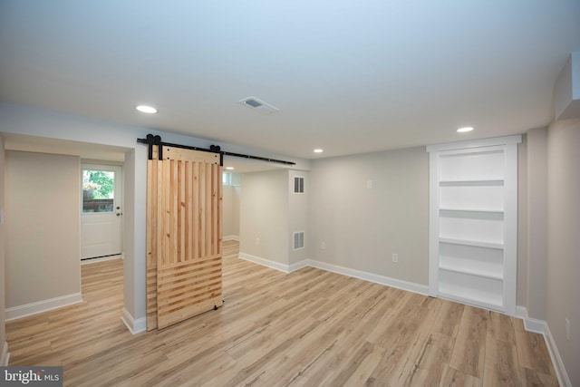 basement with light wood-style floors, recessed lighting, a barn door, and visible vents