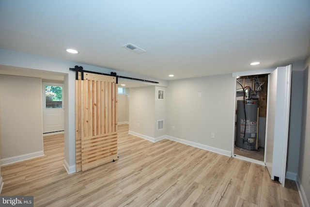 below grade area featuring visible vents, gas water heater, a barn door, and light wood-style floors