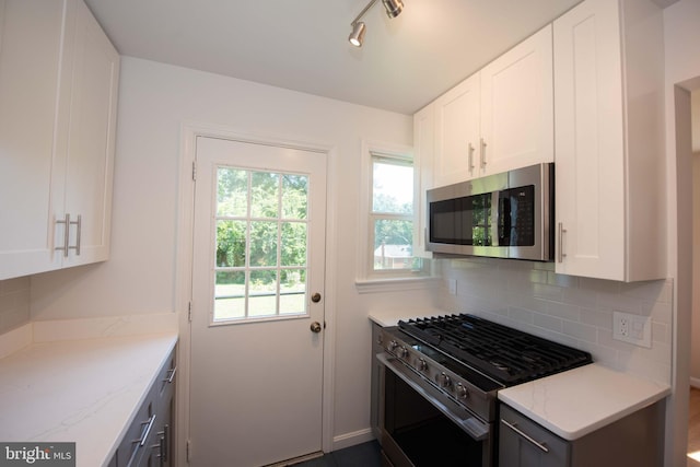 kitchen featuring decorative backsplash, white cabinetry, light stone countertops, and stainless steel appliances
