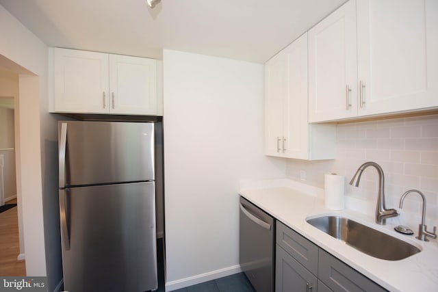 kitchen with tasteful backsplash, white cabinetry, a sink, stainless steel appliances, and baseboards